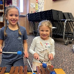 Two girls holding mallets playing a xylophone together. 